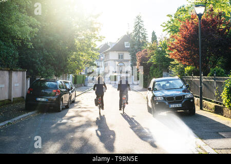 Strasbourg, France - May 19, 2017: Rear view of couple on bicycle on French street early in the morning with sunlight flare  Stock Photo