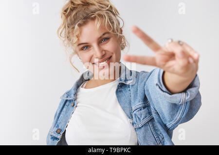 Optimistic lucky energized good-looking female fitness trainee blond curly haircut blue eyed show victory gesture give peace sign smiling broadly Stock Photo