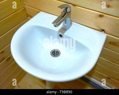 Water tap, single lever metal mixer, white ceramic washbasin on wooden wall. Stock Photo