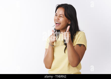 Hey what up. Friendly and outgoing carefree playful polynesian tattooed girl in yellow t-shirt making finger pistols and pointing at camera winking Stock Photo