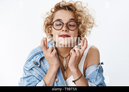 Close-up shot of hopeful excited and upbeat cute dreamy girl with short stylish haircut close eyes and smiling as making wish cross fingers for good Stock Photo