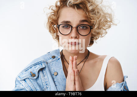 Close-up shot of cute pouting girl begging for favour, making silly face being in need holding hands in pray while asking apology or lend money Stock Photo