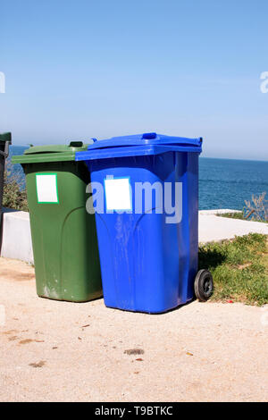 Trash can, garbage bin, recycling bin in tourist complex by sea, side of road waiting to be picked up by garbage truck. Blue and green containers. Stock Photo