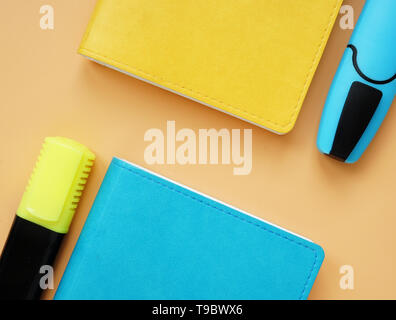 Top view of blue and yellow notepads and markers on an orange desk. Colorful office supply. Stock Photo