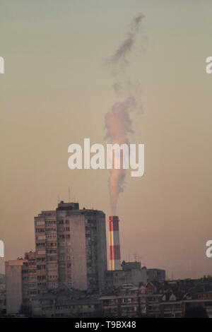Smoking from industrial chimneys of heating plant emits smoke, smog at sunset in city, pollutants enter atmosphere. Environmental disaster. Stock Photo