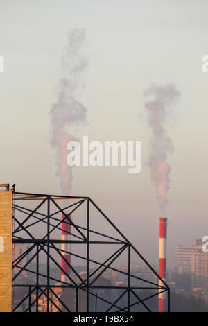 Smoking from industrial chimneys of heating plant emits smoke, smog at sunset in city, pollutants enter atmosphere. Environmental disaster. Stock Photo