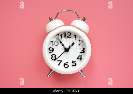 White alarm clock on a pink surface. Stock Photo