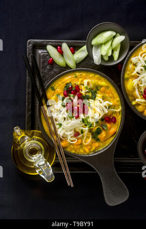 laksa with pumpkin and coconut milk, rice noodles, broccoli and pomegranate seeds in portioned black plates on a dark background. healthy vegan dish Stock Photo