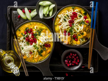 laksa with pumpkin and coconut milk, rice noodles, broccoli and pomegranate seeds in portioned black plates on a dark background. healthy vegan dish Stock Photo