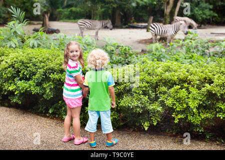 Family watching zebra in zoo. Boy and girl in tropical safari park during summer vacation in Singapore. Kids watch horse. Brother and sister learn abo Stock Photo