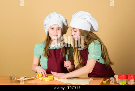 Young bakers following baking recipe. Small bakers rolling paste on kitchen table. Little girls baking cookies in baker shop. Kneading dough with baker flour. Stock Photo