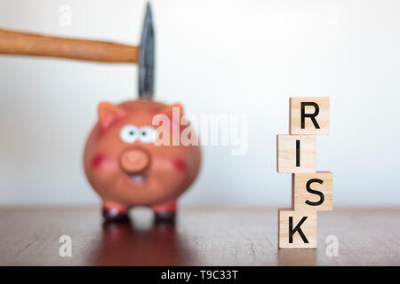 Hand holding a hammer above a Piggy bank and Risk word written on wooden cubes
