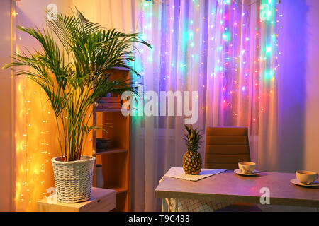 Decorative Areca palm in room near window with fairy lights Stock Photo