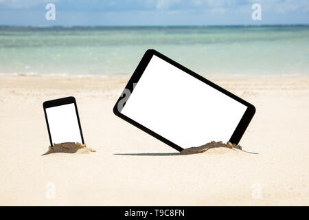 Mobile Phone And Digital Tablet Dig On Sandy Beach Near The Idyllic Sea Stock Photo