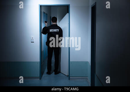 Rear View Of Male Security Guard With Flashlight Standing In Corridor Of The Building Stock Photo