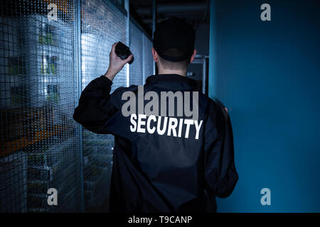 Rear View Of A Security Guard Standing In The Warehouse Holding Flashlight Stock Photo