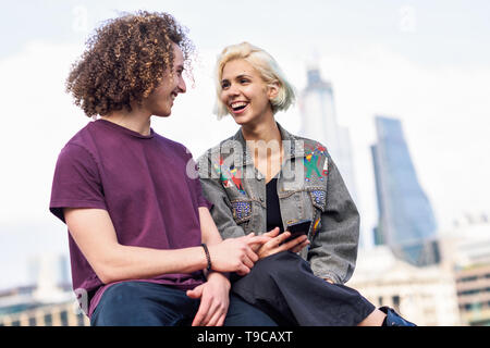 Happy couple talking sitting near River Thames. Stock Photo