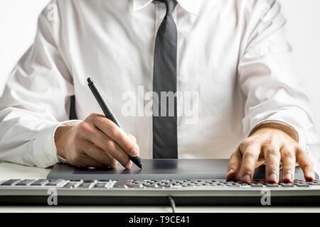 Close-up of the hands of a skilled male designer wearing white shirt and black tie while drawing on a graphics tablet, placed on the desk, next to a c Stock Photo