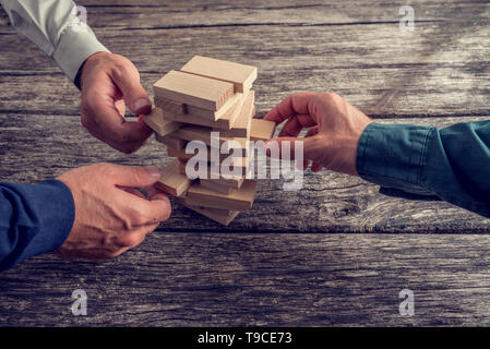 Three Businessmen Hands Playing Wooden Tower Game on Top of a Rustic Wooden Table. Conceptual of Teamwork, Strategy and Vision. Stock Photo