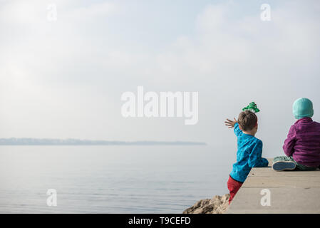 Two toddler boys sitting on a pier looking and waiving into the distance on an autumn day. Stock Photo