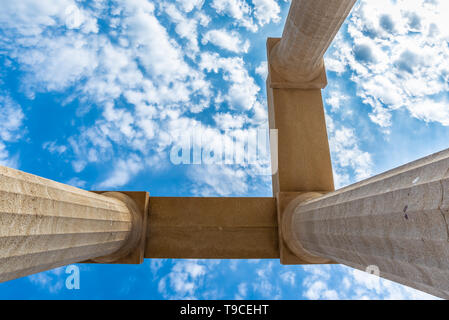 View from below of three ancient pillars against a blue sky with white clouds. Stock Photo