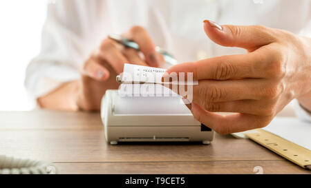 Closeup of a woman holding a printout receipt as it comes out of adding machine while she uses it to make calculations. Stock Photo