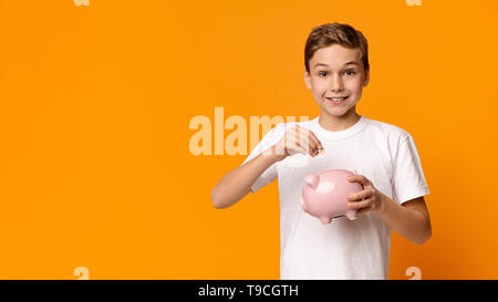Smiling little boy putting money into piggy bank Stock Photo