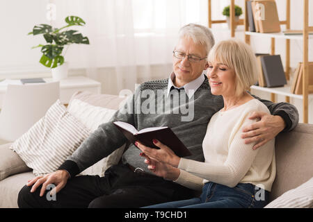 Loving Senior Couple Reading Book Together In Living Room Stock Photo