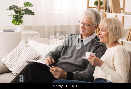 Elder Man Holding Book And Showing Illustration To His Wife Stock Photo