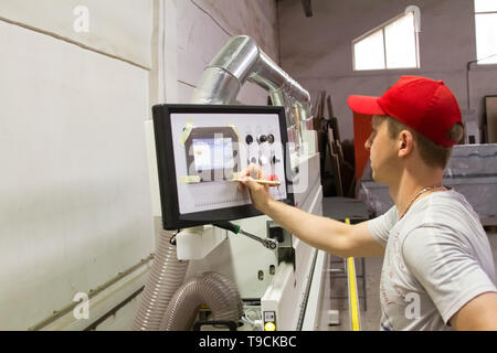A male engineer controls the work of the machine in the furniture shop. Stock Photo