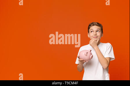 Teen boy with piggy bank dreaming about some things he can buy Stock Photo