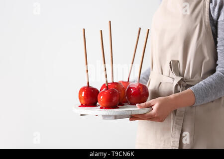 Woman holding board with delicious candy apples on light background Stock Photo