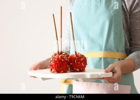 Woman holding board with delicious candy apples on light background Stock Photo