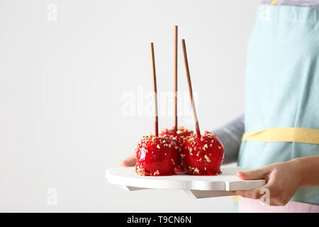 Woman holding board with delicious candy apples on light background Stock Photo