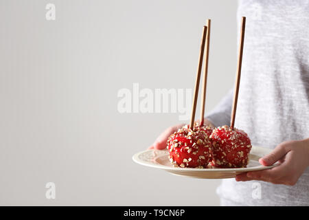 Woman holding plate with delicious candy apples on light background Stock Photo