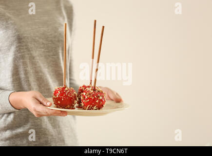 Woman holding plate with delicious candy apples on light background Stock Photo