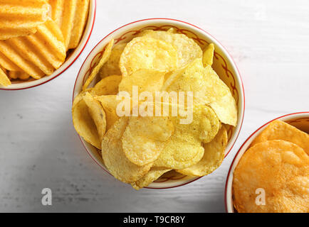 Bowls with tasty crispy potato chips on white wooden table Stock Photo