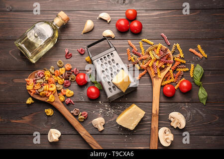 Different raw pasta with vegetables and cheese on dark wooden table Stock Photo