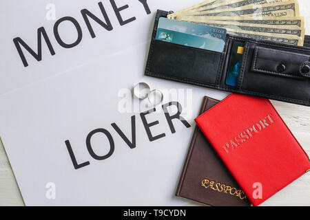 Wedding rings, wallet with dollars, passports and card with text MONEY LOVER on table. Marriage of convenience Stock Photo