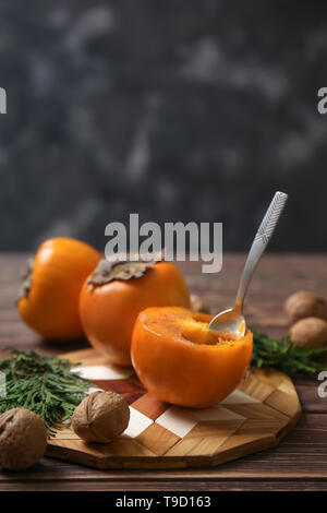 Tasty ripe persimmons with walnuts and cutting board on wooden table Stock Photo
