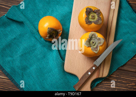 Tasty ripe persimmons with cutting board on wooden table Stock Photo