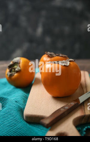 Tasty ripe persimmons with cutting board on table Stock Photo