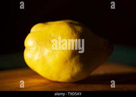 A Quince fruit on a wooden chopping board with natural side light. Stock Photo