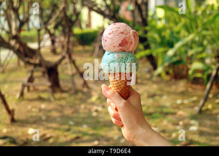 Two scoops of ice cream cone in woman's hand with blurry sunshine garden in background Stock Photo