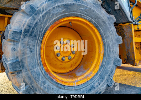 Close up of the wheel of a yellow loader parked on the road on a sunny day Stock Photo