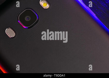 A fragment of the cell phone case in black with blue and red backlight. The phone lies on the black technological surface of the camera up with blue a Stock Photo