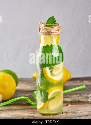 summer refreshing drink lemonade with lemons, mint leaves, lime in a glass bottle on a wooden table Stock Photo