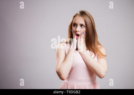 Beautiful young woman wears a pink dress and stares in the direction on gray background with copy space, girl is delighted with product, cosmetics, gi Stock Photo