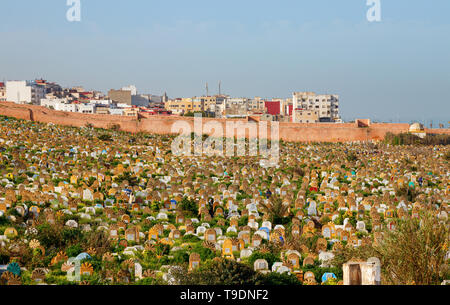 Cemetery with graves and tombstones, covered with grass at the coast with residential buildings in the background on a sunny afternoon. Rabat, Morocco. Stock Photo