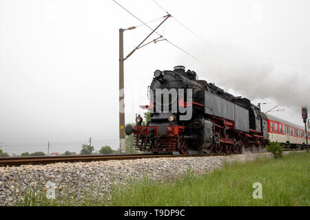 Vintage steam engine locomotive speeding on railroad tracks curve and blowing heavy white smoke. Stock Photo